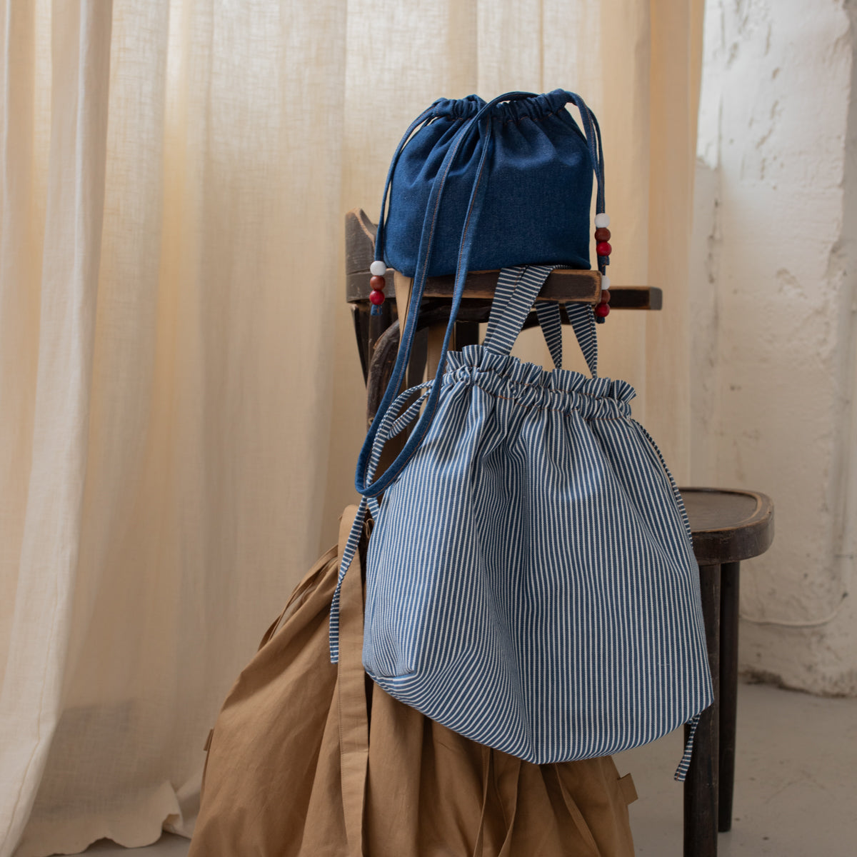 Trois sacs bourse Manhattan en denim bleu et à rayures bleues suspendus à une chaise – patron de couture Ikatee