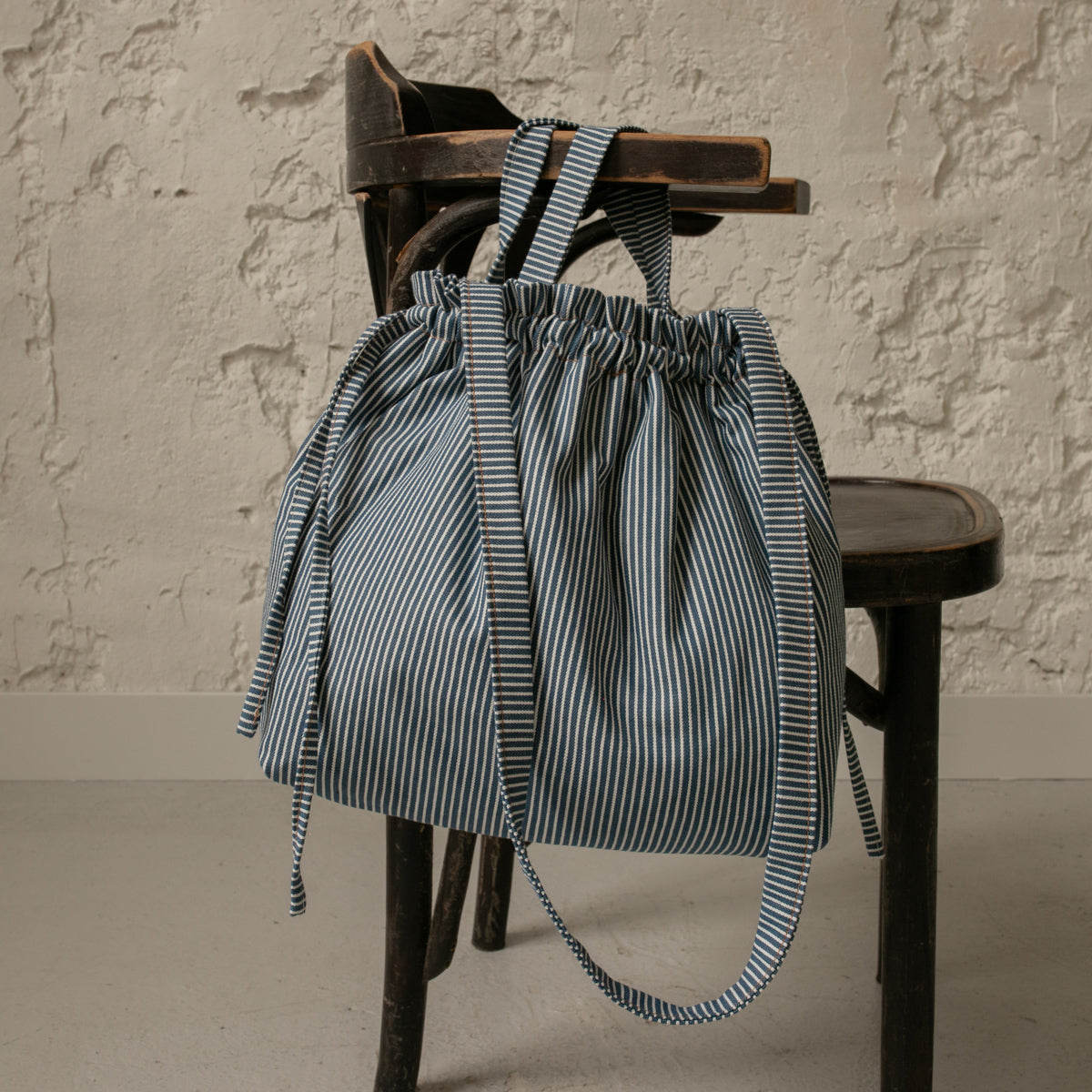 Sac bourse Manhattan à rayures bleues et blanches avec bandoulière, suspendu à une chaise – patron de couture Ikatee